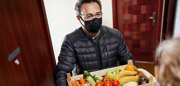 Homme avec  un masque qui livre à domicile des fruits et légumes à une personne âgée 