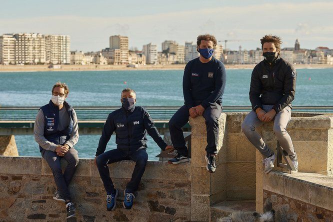 Les skippers Benjamin Dutreux, Manuel Cousin, Arnaud Boissières et Sébastien Simon assis sur un muret le long du port des Sables d'Olonne